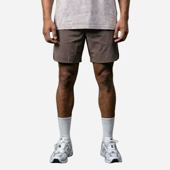 Man wearing a light gray t-shirt and shorts standing against a concrete wall.