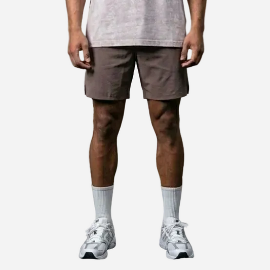 Man wearing a light gray t-shirt and shorts standing against a concrete wall.