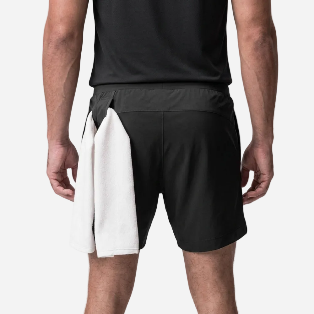 Person wearing black athletic shorts holding a white towel on a light gray background