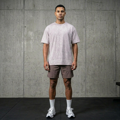 Man wearing a light gray t-shirt and shorts standing against a concrete wall.